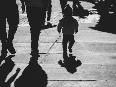 a black and white photo of a little girl walking with her parents