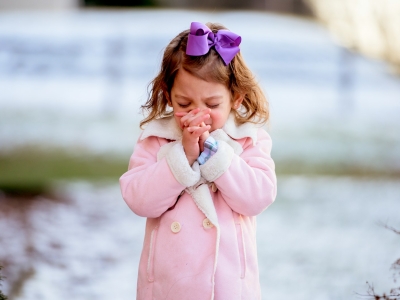 a little girl in a pink coat holding her hands together